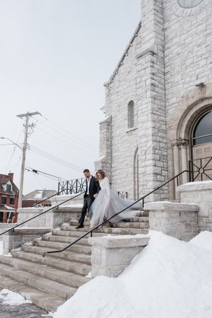 Winter wedding scene with couple on snowy church steps featuring gothic stone architecture.