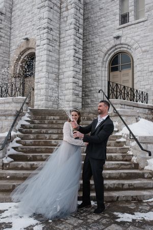 Winter wedding scene on snowy stone church steps with elegant couple.