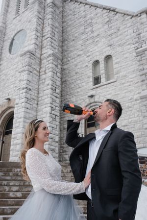 Couple sharing celebratory drinks on church steps during wedding photoshoot.