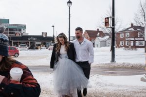 A couple walking together in a snowy winter street scene wearing formal attire including a tulle dress.