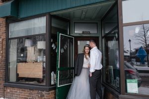 Couple in wedding attire standing outside a small town storefront.