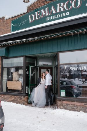 A wedding couple poses in front of the historic Demarco building on a snowy day.