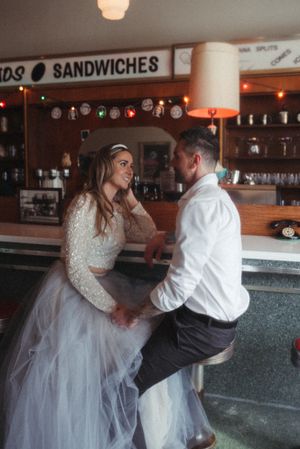A casual moment at a retro diner counter with two people in wedding attire.