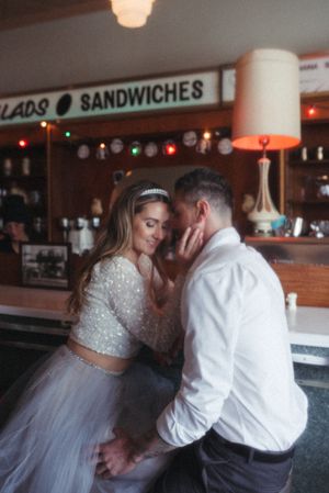 A romantic moment between newlyweds at a retro diner with string lights in the background.