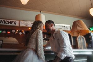 A couple in wedding attire shares an intimate moment at a retro diner counter.