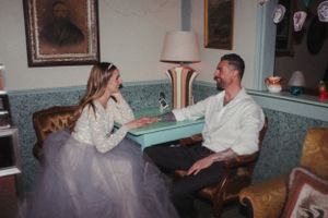 A couple in wedding attire sits together in a vintage-style room with blue walls.