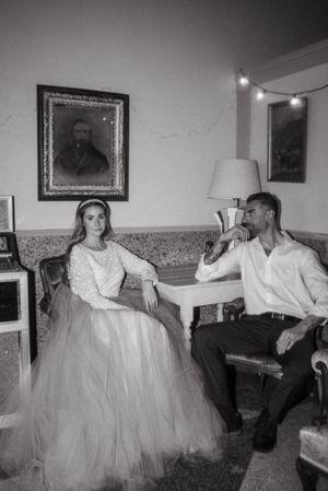Black and white photo of a couple relaxing on a vintage couch beneath framed artwork.