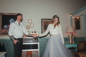Couple in wedding attire sharing playful moment near piano in retro-styled room.