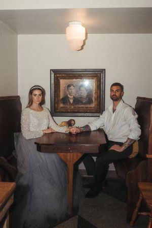 Vintage-inspired portrait of couple at wooden table with antique photograph and lighting.