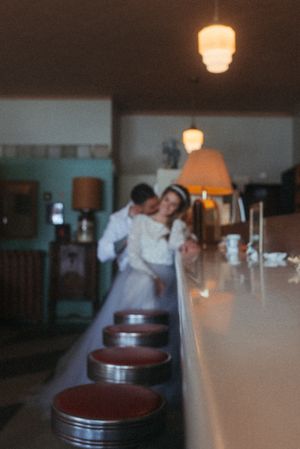 A couple embraces in a dimly lit retro diner setting with vintage bar stools.