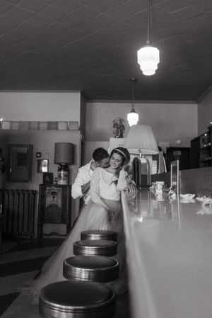 A vintage black and white photo showing a couple embracing at a retro diner counter with bar stools.