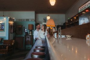 A loving couple in wedding attire stands together at a vintage diner counter.