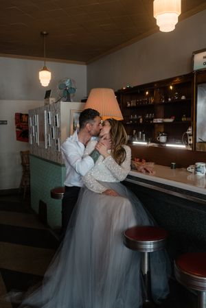 Intimate wedding moment captured in retro diner setting with vintage decor and lighting.
