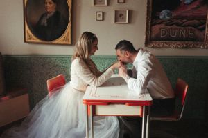 A romantic scene at a retro diner booth with two people in wedding attire sharing a tender moment.