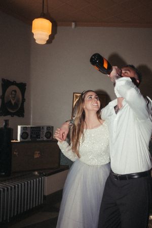 A couple celebrates with champagne in a dimly lit vintage-style room with retro decor.