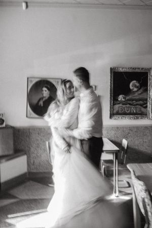 A black and white photograph of a dancing couple in formal attire inside a vintage room with framed artwork.