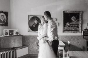 Black and white photo of couple dancing in vintage-style room with portraits on wall.