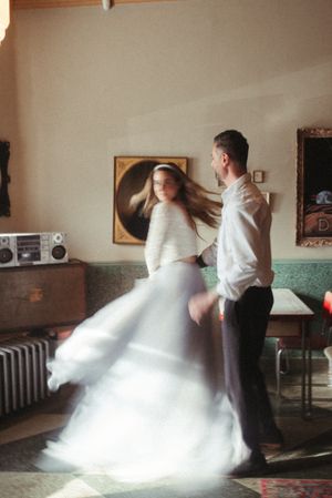 A couple dances in a vintage-style room with flowing white dress and retro decor.