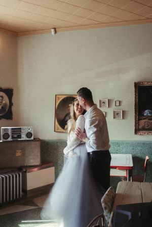 A couple shares an intimate dance moment in a vintage room with a retro boombox and framed artwork on the wall.