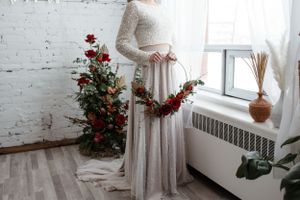 An elegant wedding dress with lace details and long sleeves is captured near floral decor and a window.