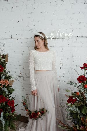 Bridal fashion with sparkly crop top and tulle skirt against white brick wall with red roses.