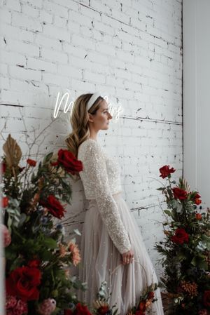 A bridal portrait against white brick wall with red roses and winter floral arrangements.