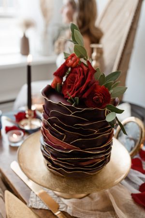 Elegant chocolate wedding cake decorated with red roses and gold accents on a display stand.