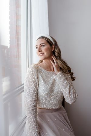 A person in a sparkly wedding top poses by a window with natural light streaming in.