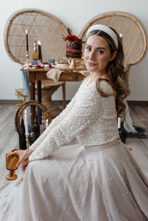 A person in a sparkly wedding dress poses in front of a decorated table with vintage decor.