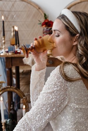 A person in a sequined dress drinking from a glass in an elegant setting.