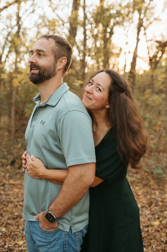 A couple shares joyful laughter together during an autumn photoshoot in a wooded setting with fallen leaves.