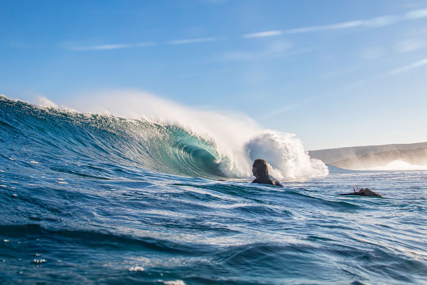 A surfer rides inside a breaking ocean wave with sunlight and spray creating a dramatic seascape.