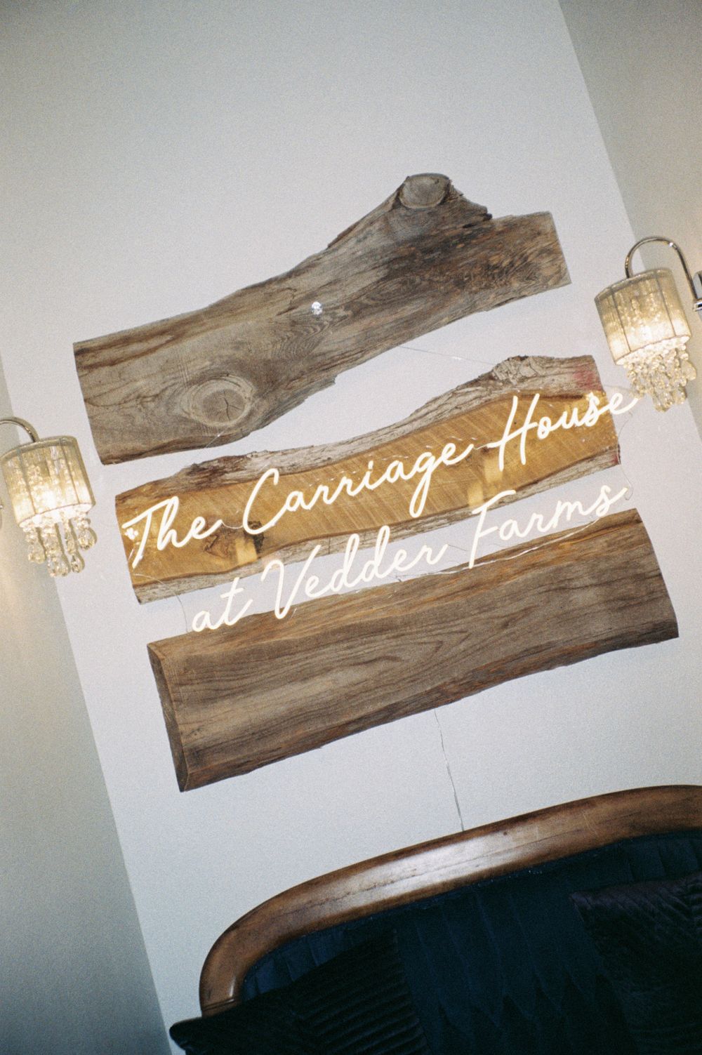 Rustic wooden sign for 'The Carriage House' with decorative crystal wall sconces mounted on white wall located at vedder farms in leesburg