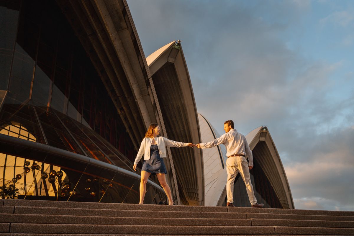couple lingering through watching each other on the stairs of Opera House in Sydney during a golden light during a proposal photoshoot