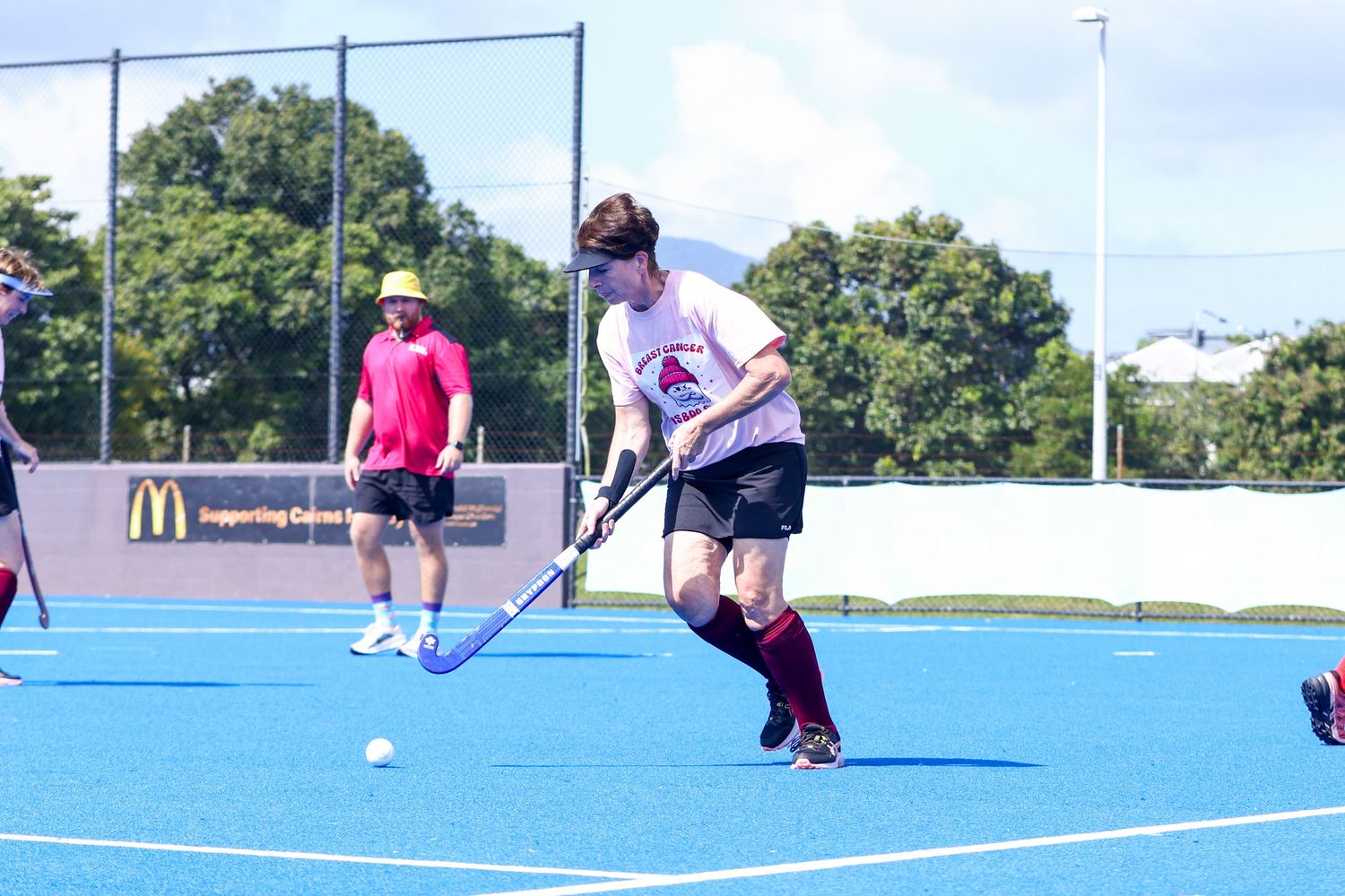 Field hockey player dribbling ball on blue turf with players in background during outdoor match.