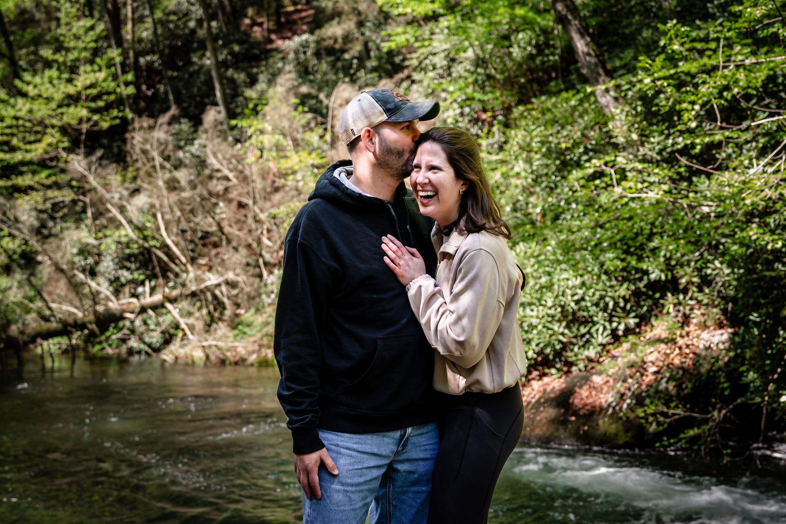 A couple enjoys tender moments together along a scenic forest waterway.