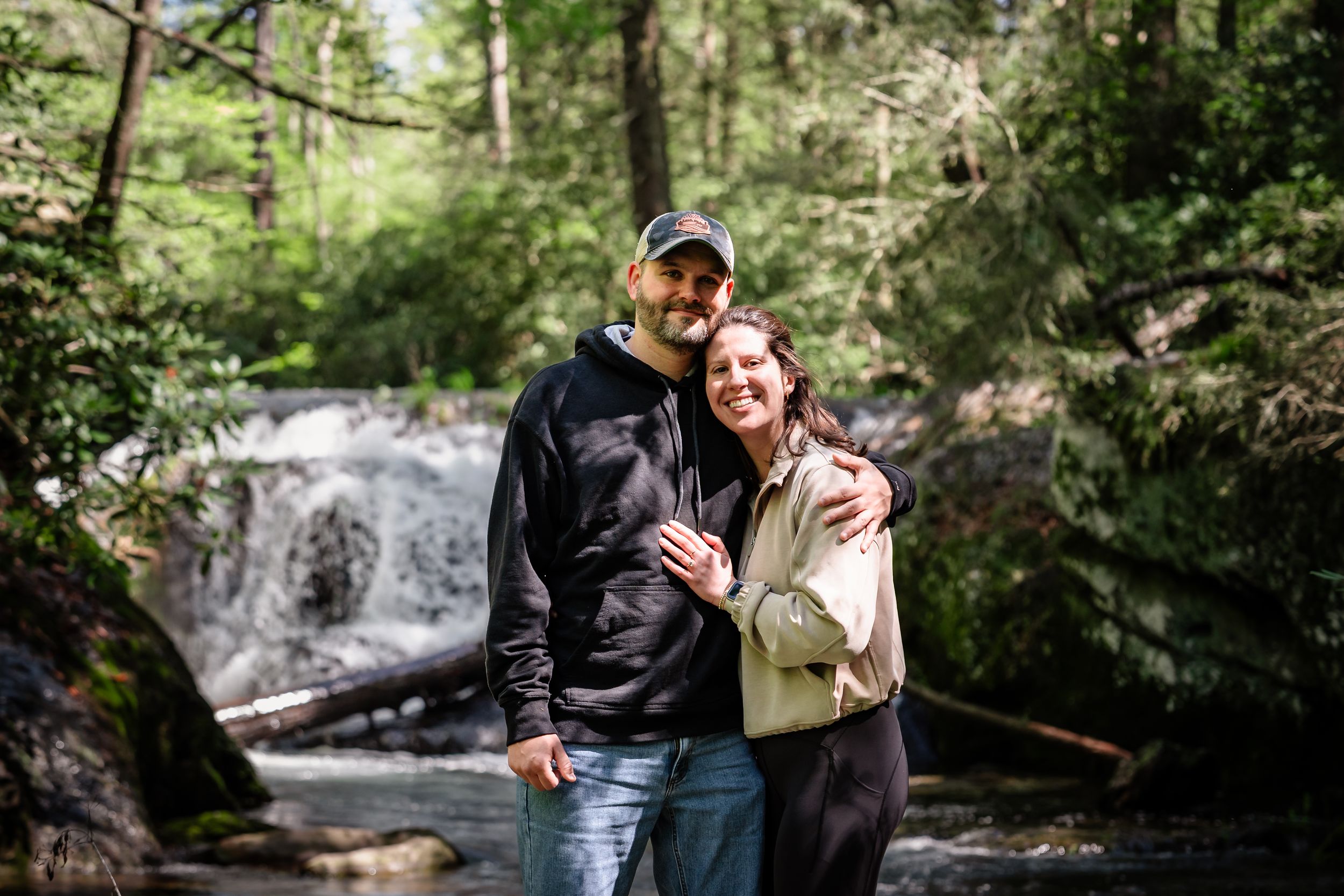 Couple enjoying a romantic moment by a scenic waterfall in a lush forest setting.