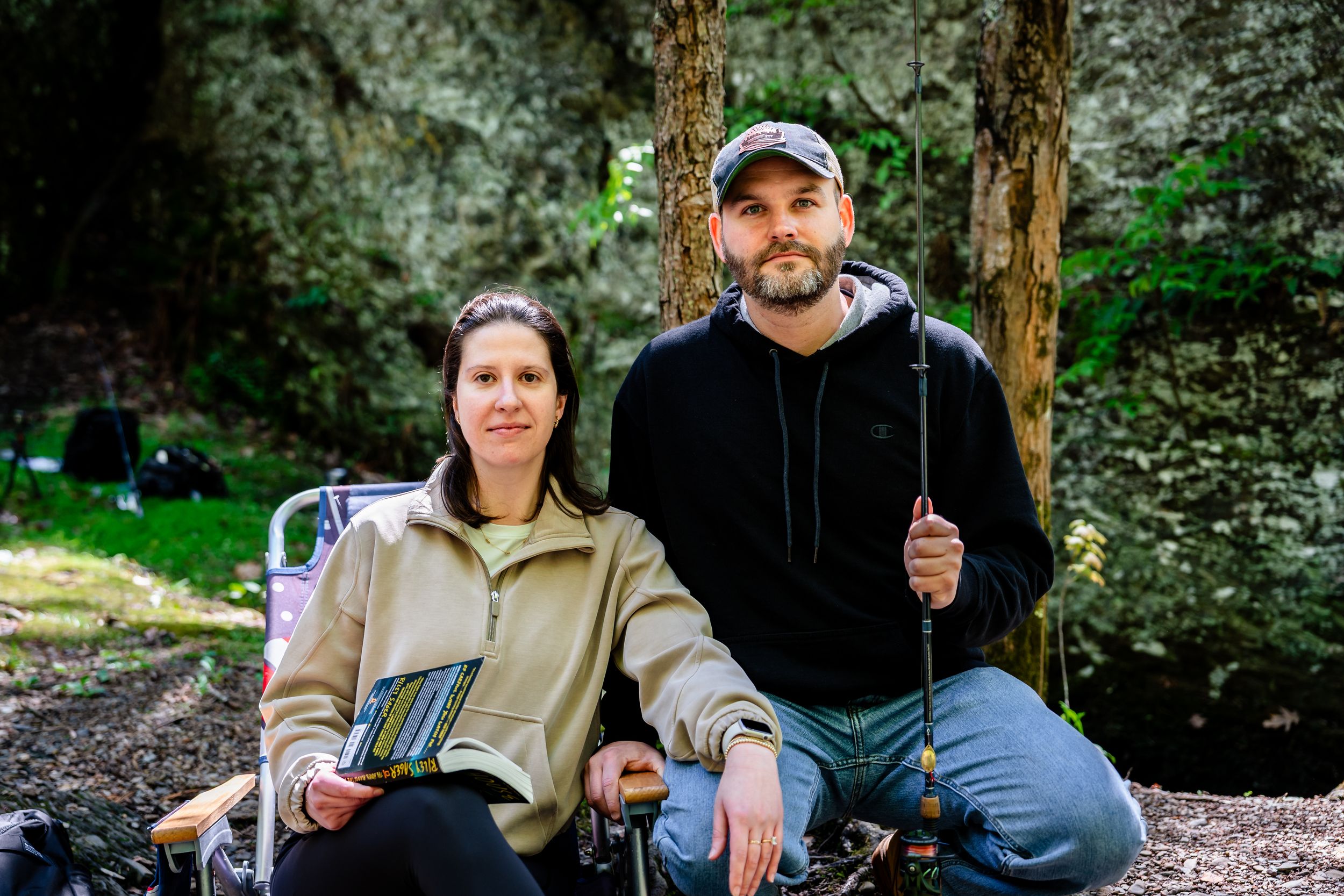 Two people sit together on rocks near a forest stream.
