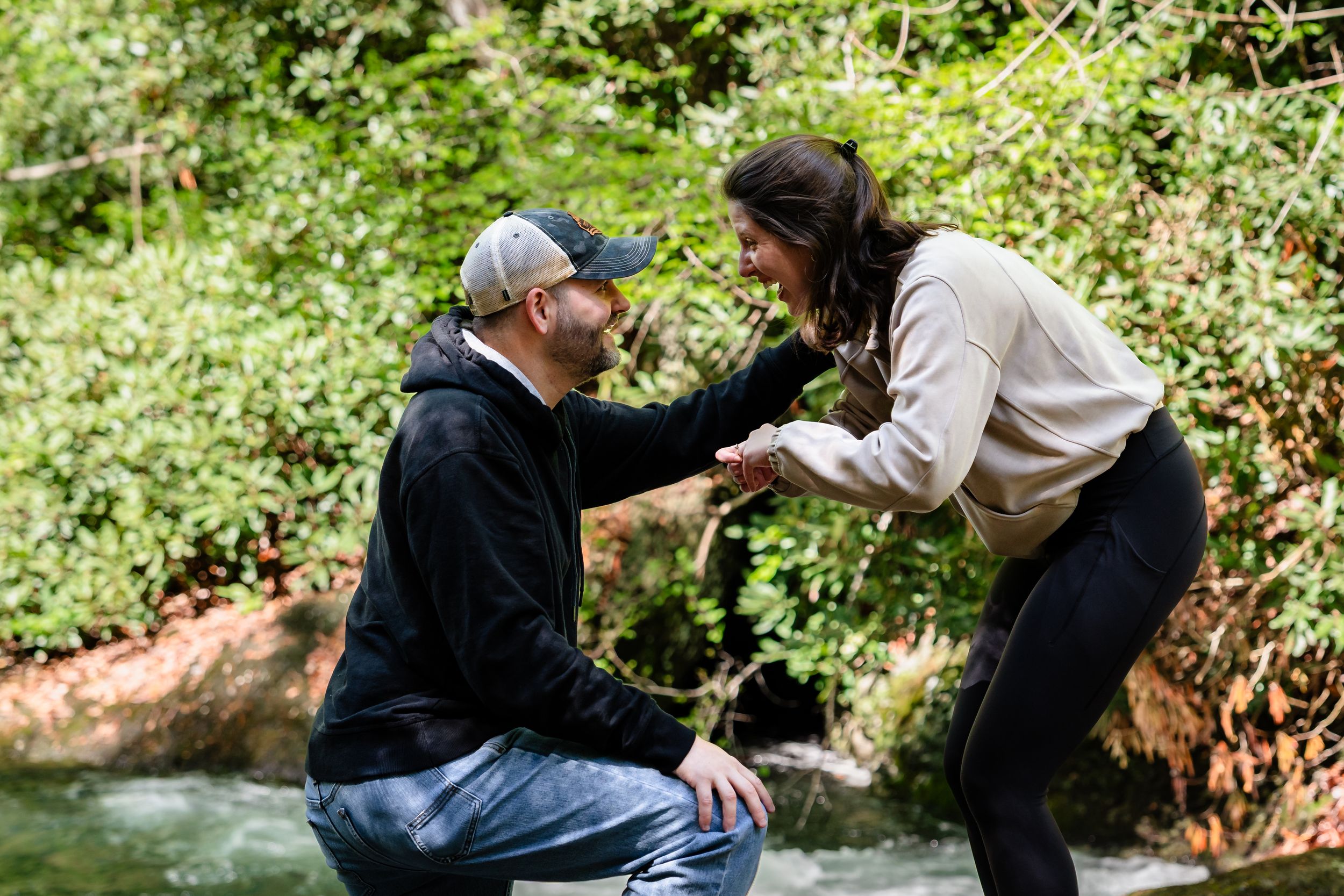 A couple shares intimate moments while sitting beside a forest stream.