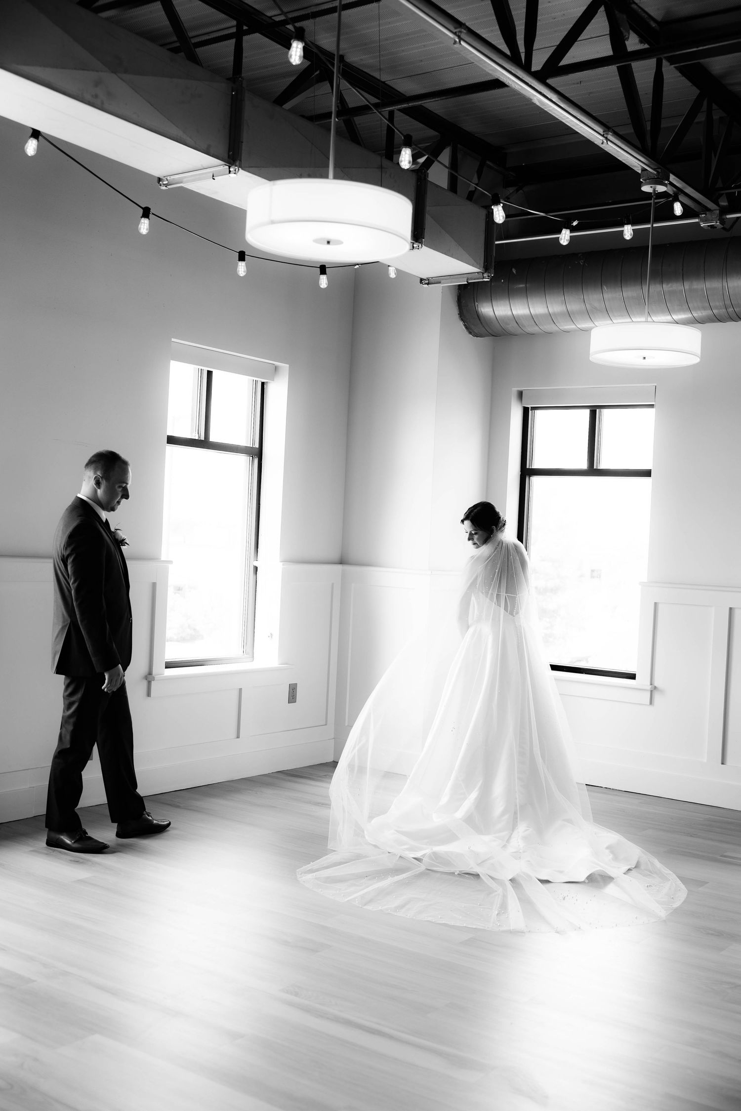 Black and white photo of a bride in a flowing gown and groom sharing a first look in an elegant venue.