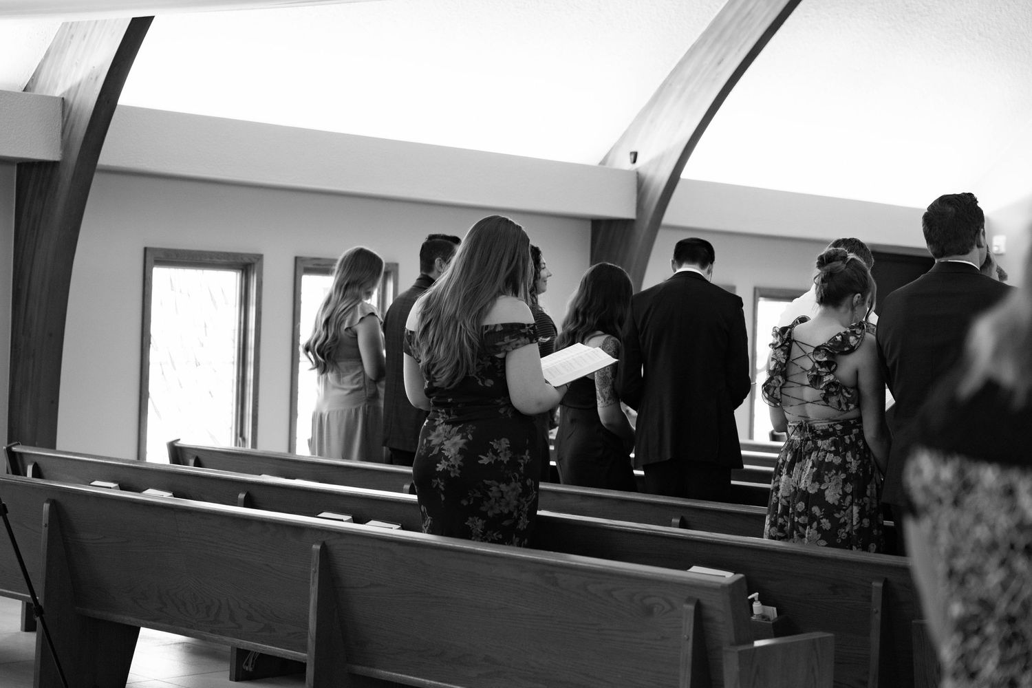 Black and white photo of wedding guests standing in church pews during a ceremony.