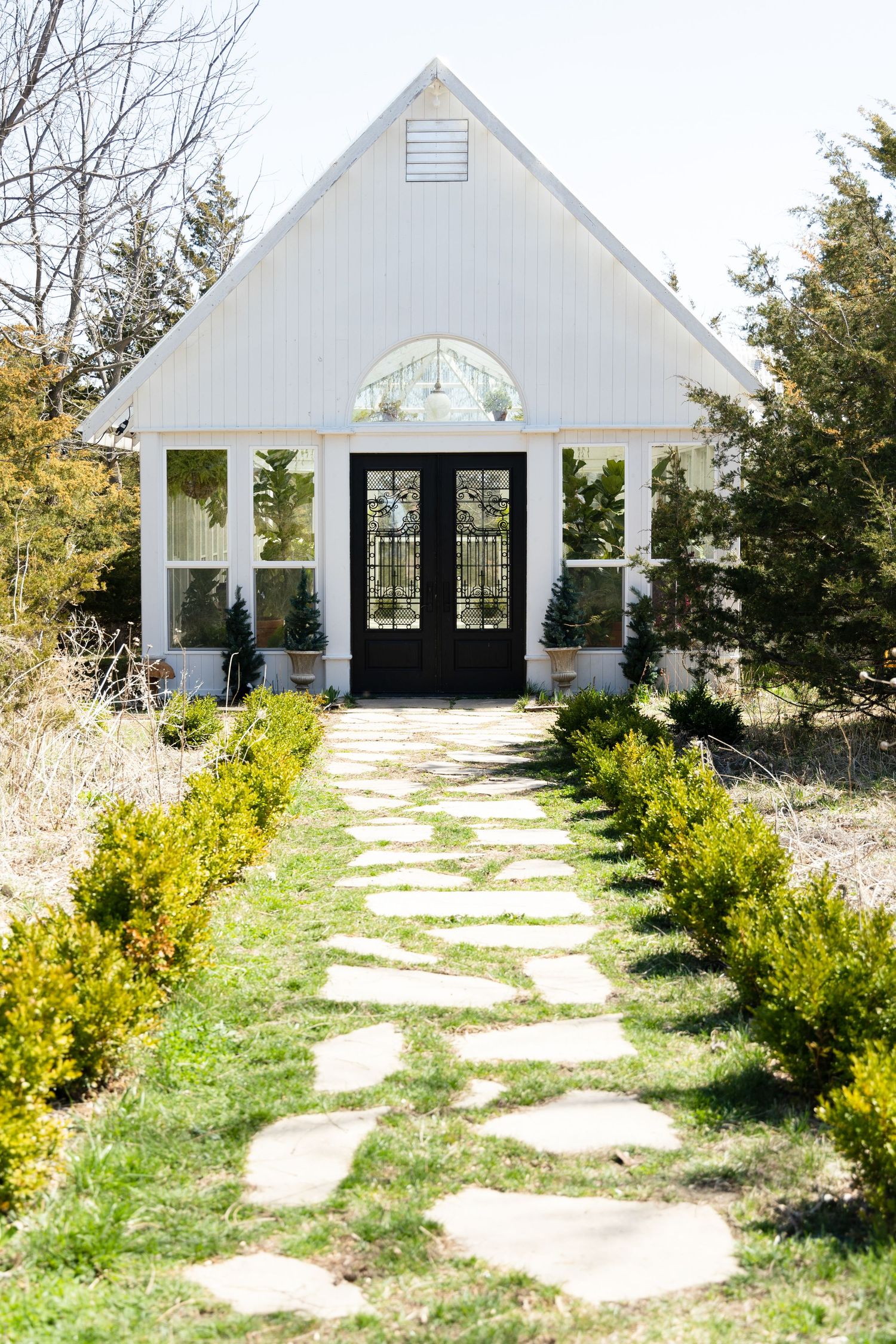 White chapel with black double doors and stone path lined with yellow flowering shrubs.
