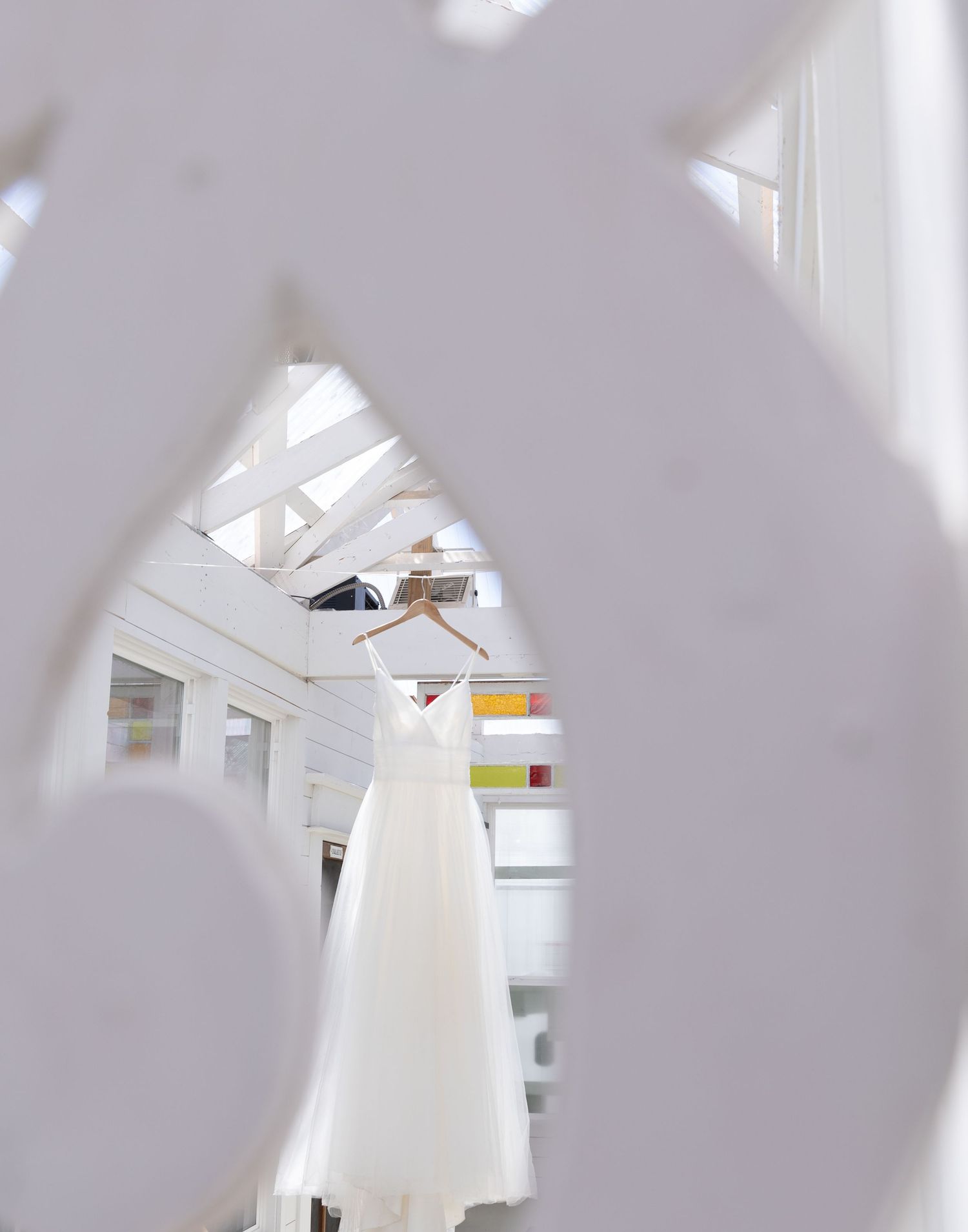 White wedding dress seen through architectural frame in bright conservatory setting.