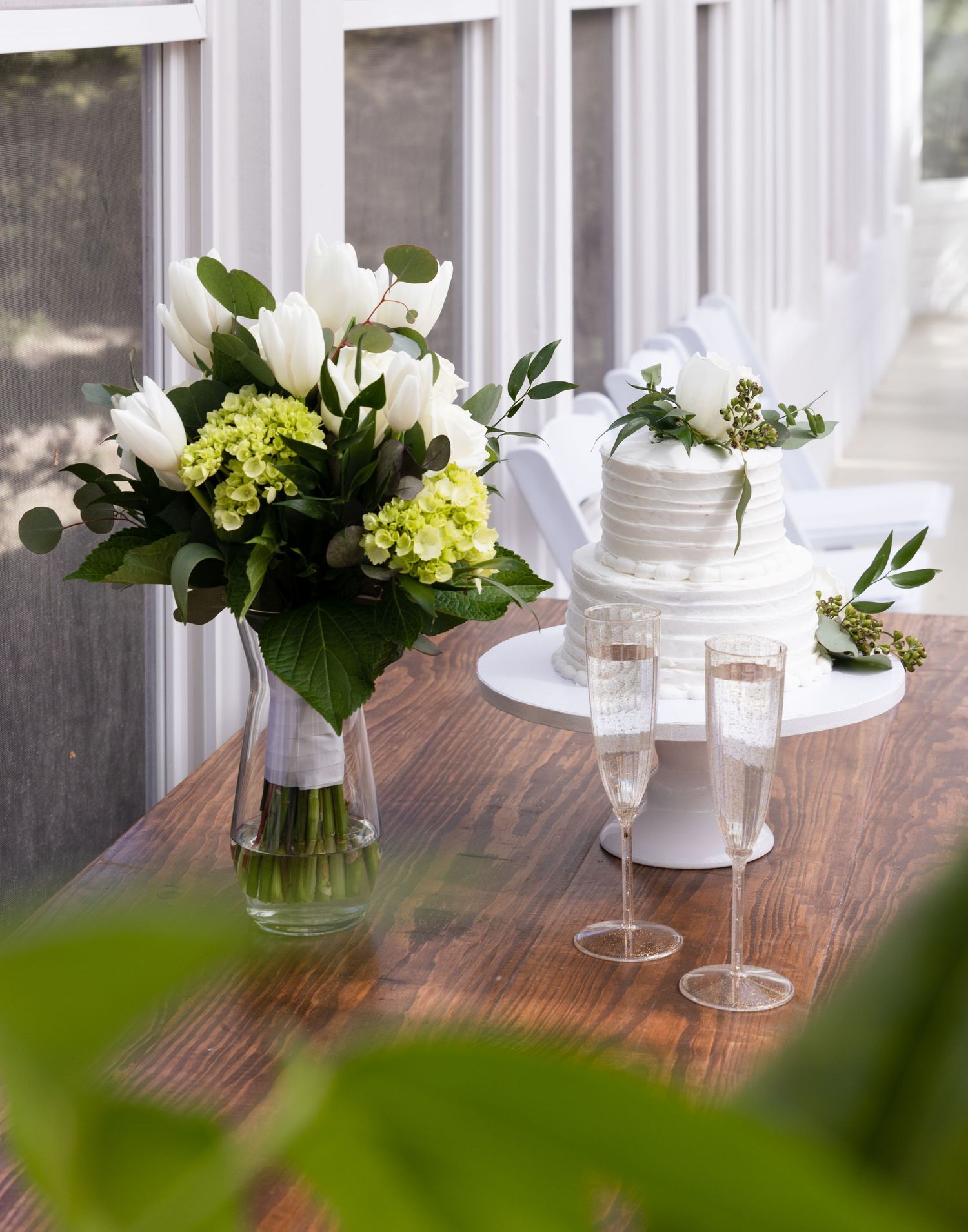 Wedding floral arrangement with white and green hydrangeas next to champagne glasses on wooden table.