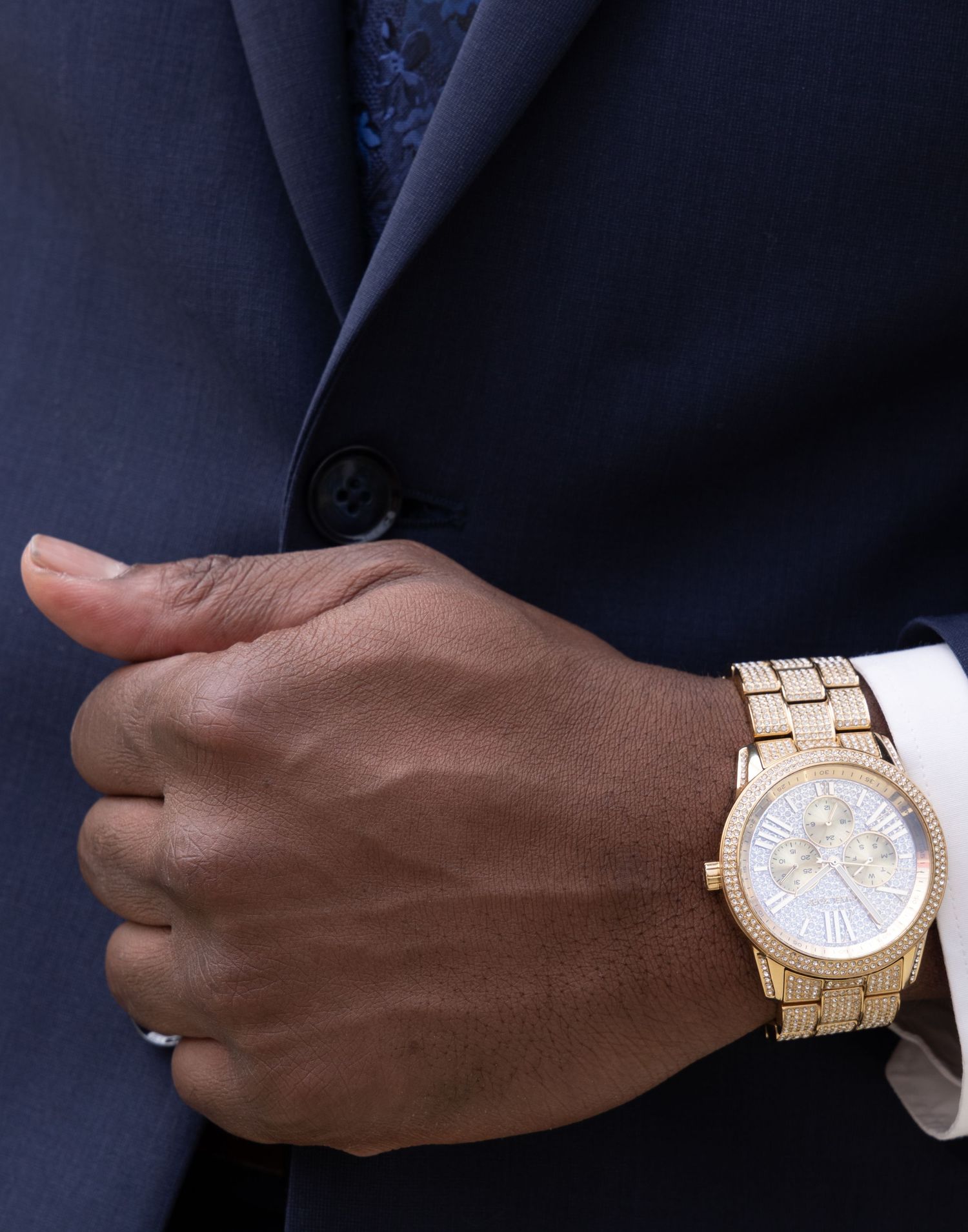 Close-up of gold watch on wrist with navy suit sleeve.