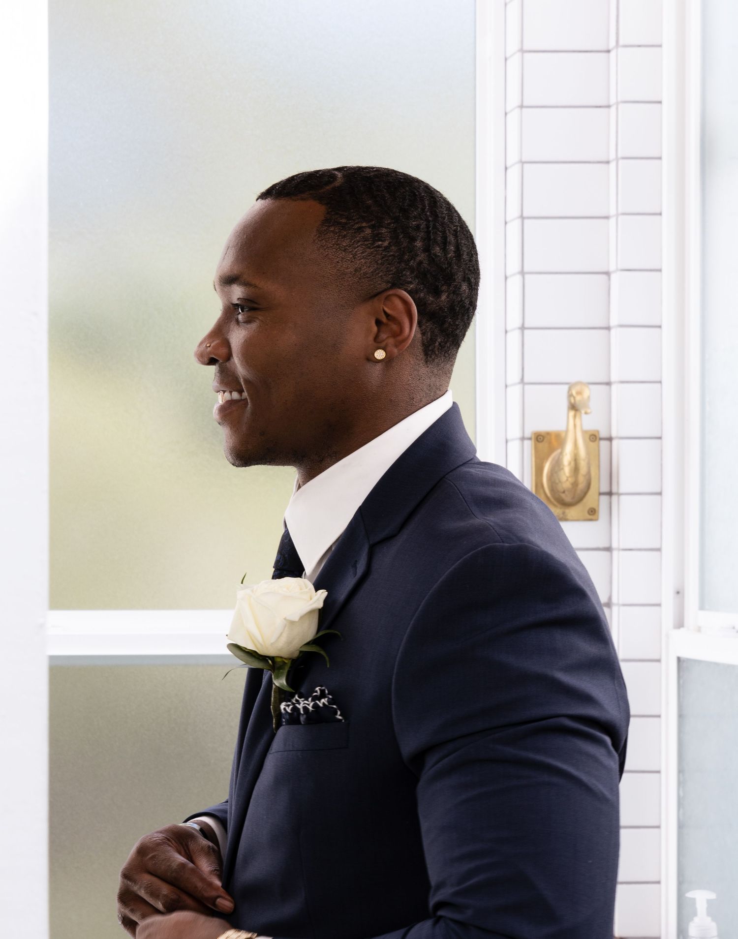 Groom in navy suit with white boutonniere poses in elegant side profile on wedding day.
