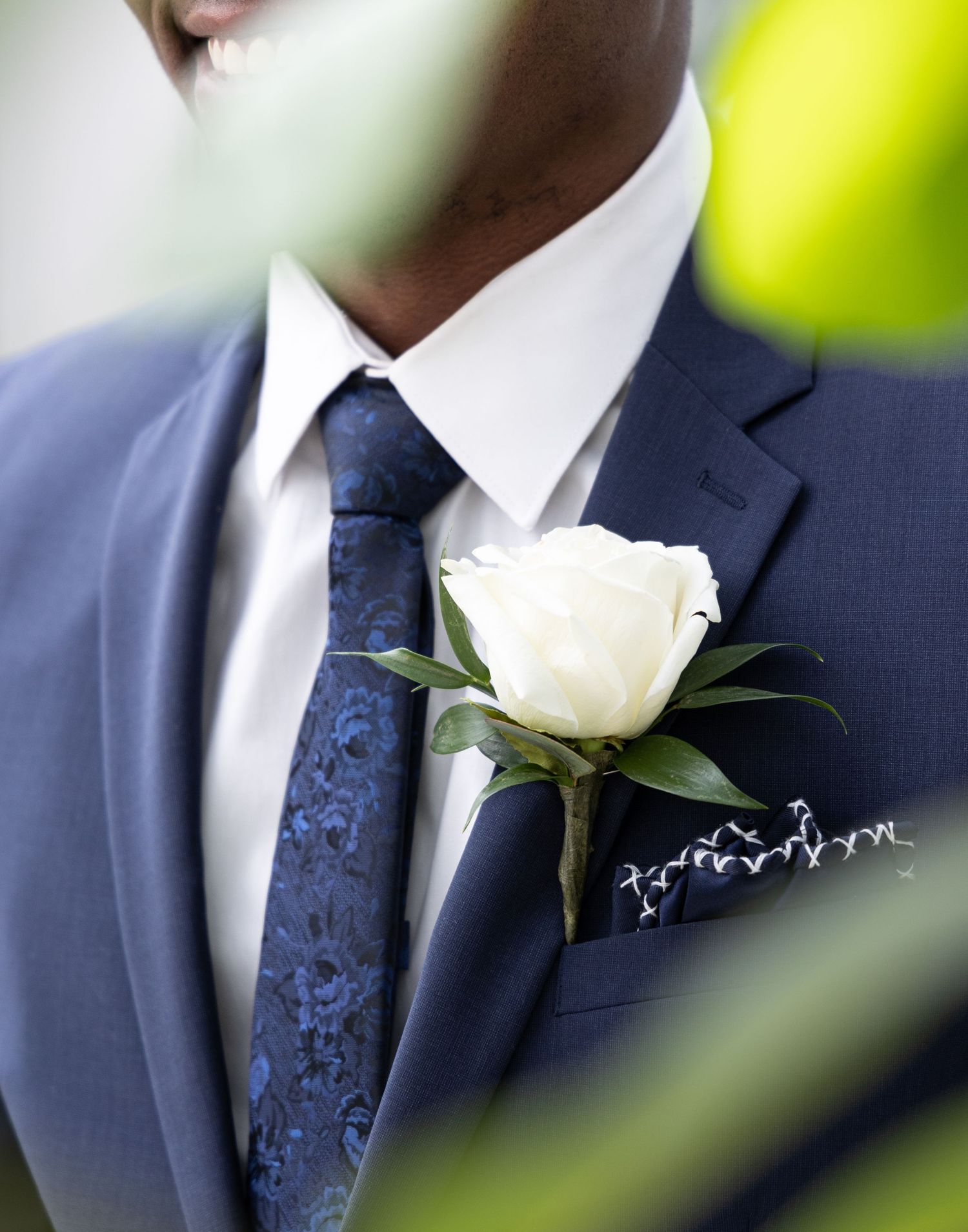 Elegant navy suit with white rose boutonniere and patterned tie detail.