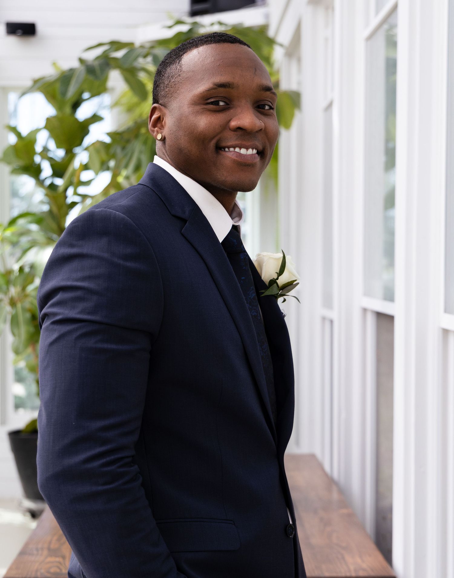 Dapper groom in fitted navy suit smiles brightly with white rose boutonniere.
