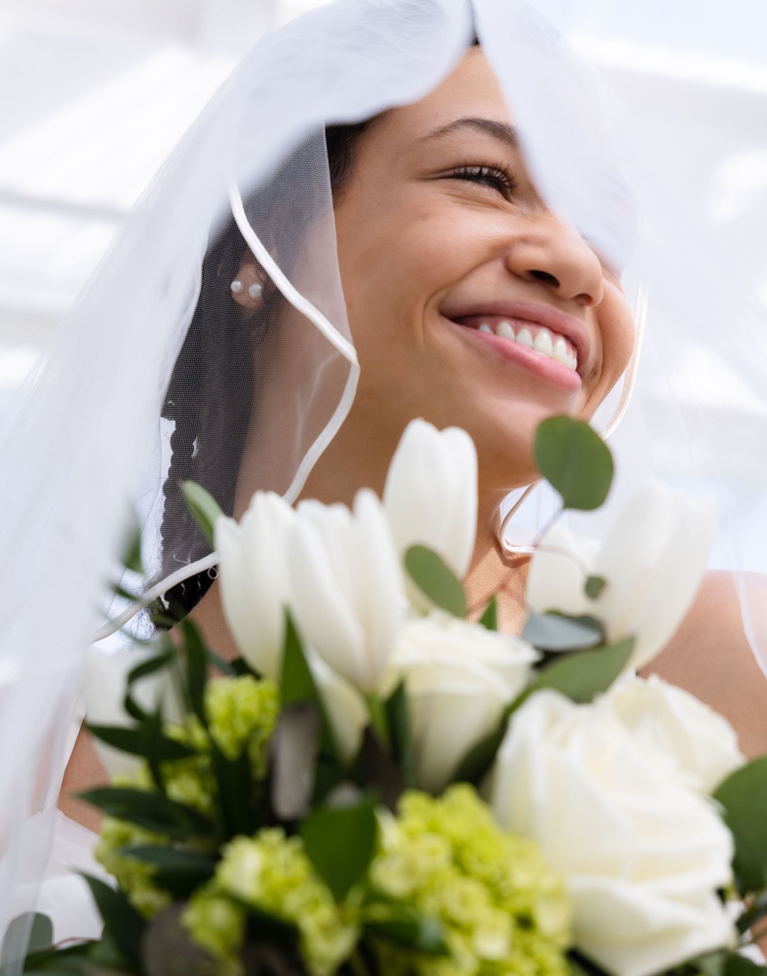 Radiant bride smiles while holding white and green bouquet under veil.