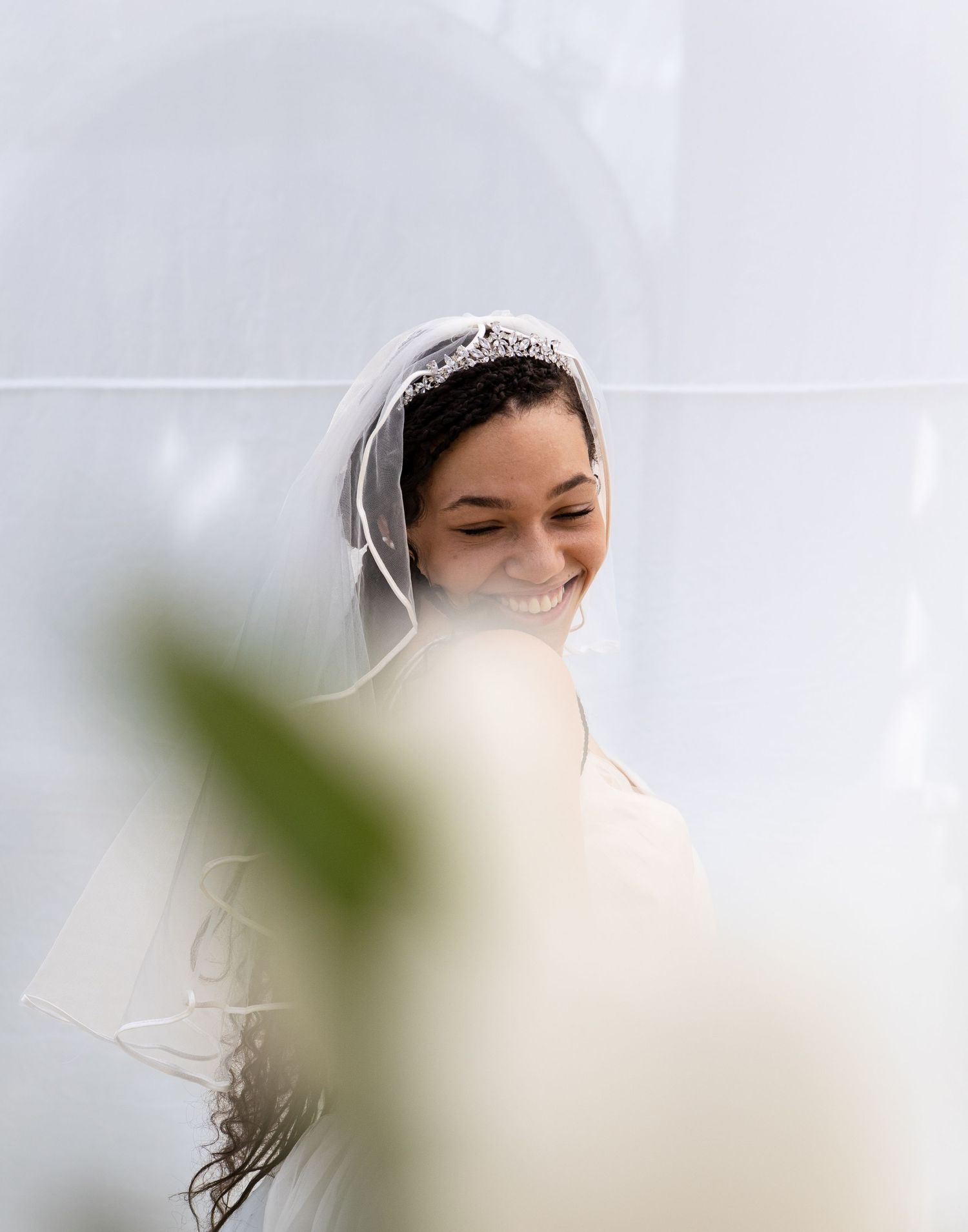 A joyful moment captured through greenery as a bride smiles in her wedding veil.